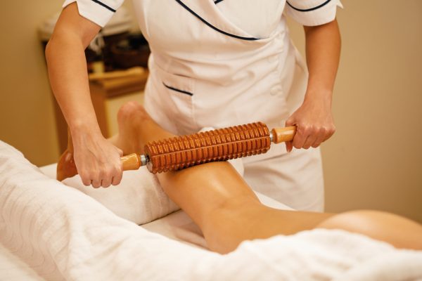 Unrecognizable woman during maderotherapy at the spa. Unrecognizable therapist performing maderotherapy on woman's legs during massage treatment at the spa.